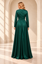 Rear view of an emerald green long-sleeve gown with a closed back neckline, ruched waist and gathered skirt.
